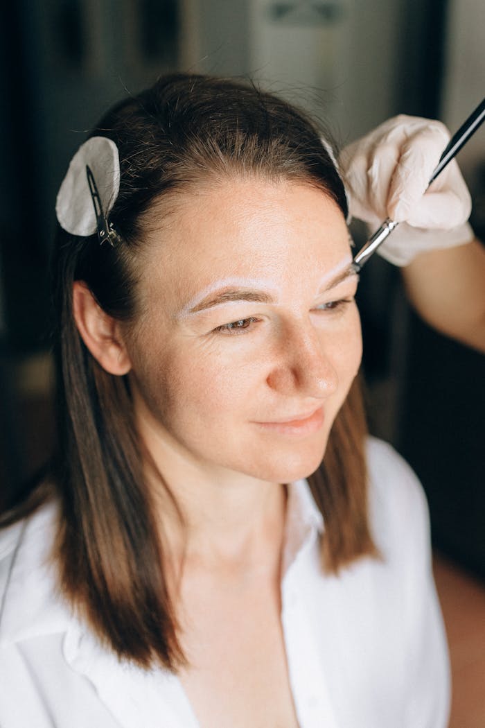Woman undergoing eyebrow contouring with a makeup brush in a salon setting.